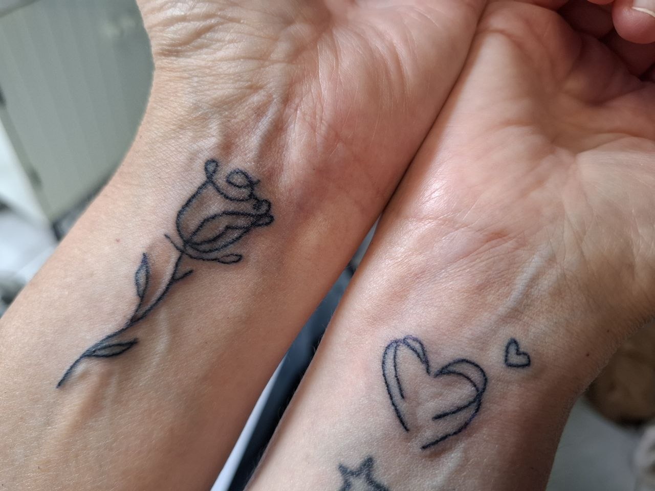 Fineline tattoo: roos en hartjes op de polsen